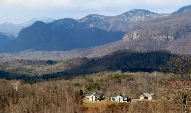 A couple homes sit in the bottom of a mountainous valley.