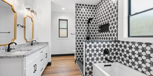 A custom bathroom in a home complete with gold-framed mirrors and an intricate black and white tile shower